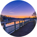 profile picture of a sunset across a waterfront or lake seen from a wooden deck